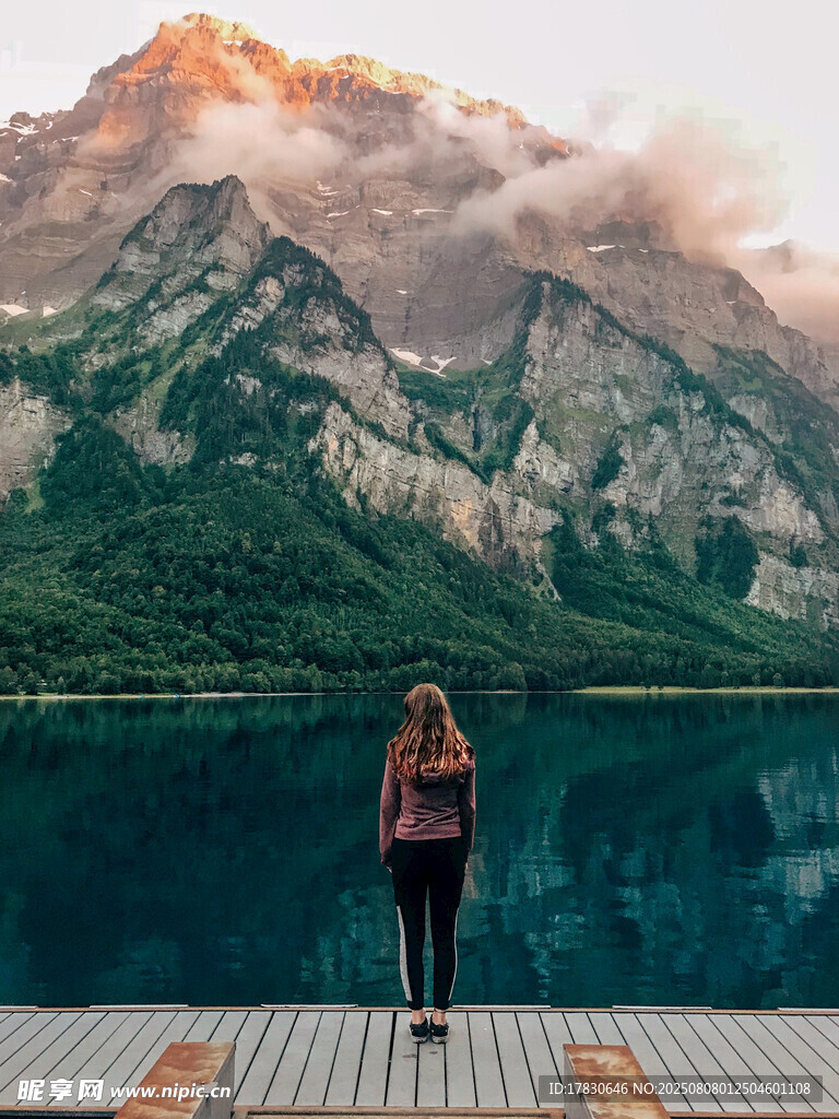 女子立于湖畔賞巍峨山景