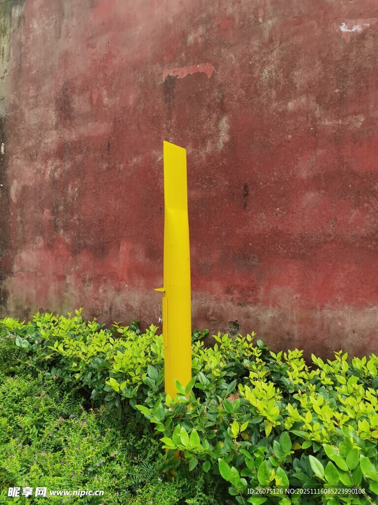 黃色標(biāo)桿立于綠植與紅墻旁