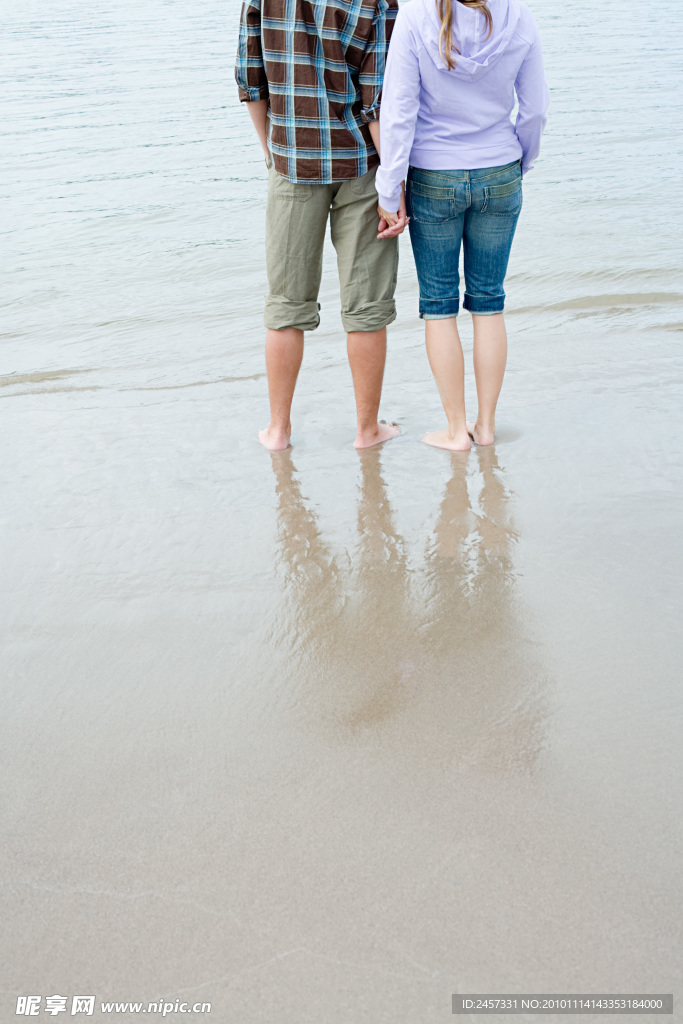 海边沙滩手拉手的情侣腿部特写