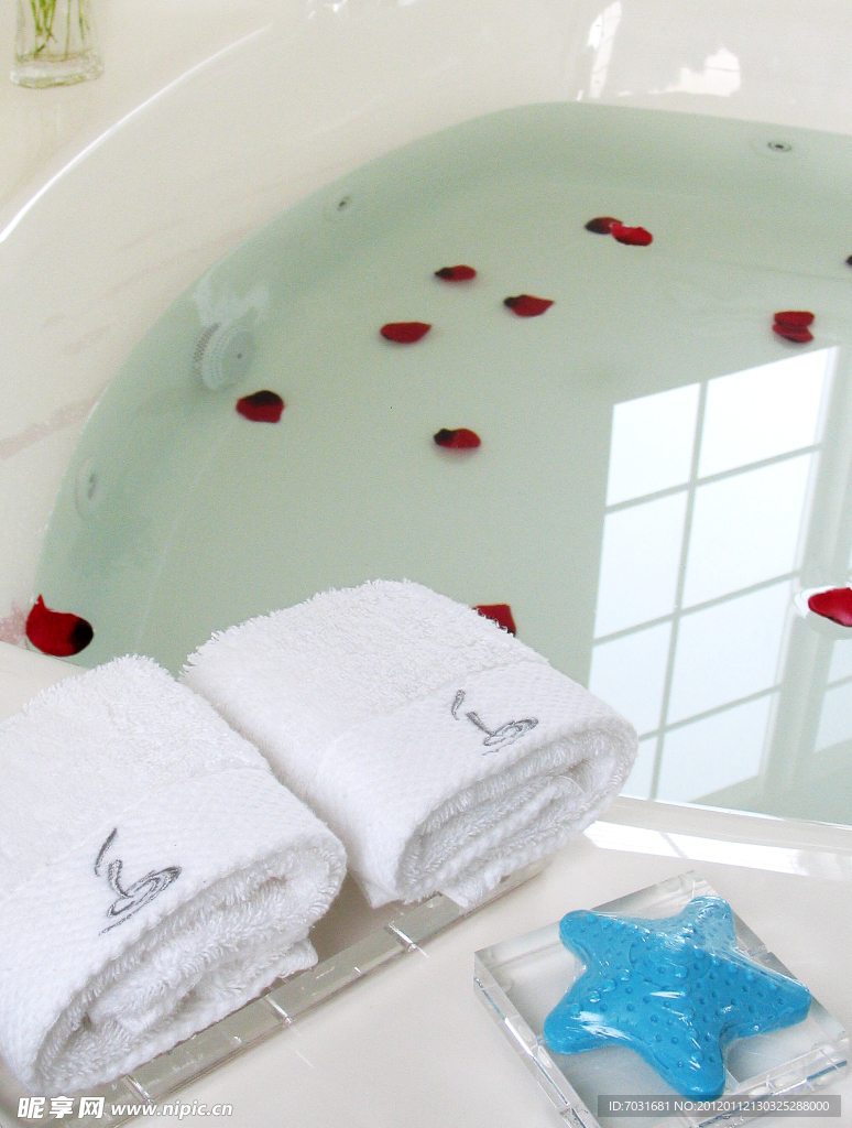 水中漂着玫瑰花瓣的浴盆旁摆放整齐的沐浴用品
