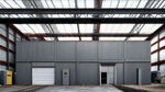 钢结构车间厂房，两层，灰色外观，长方体，一楼门口位于中间，仅有一个大门，门口有道路，二楼有窗户