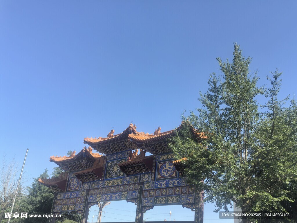 中式牌坊立于蓝天绿树间