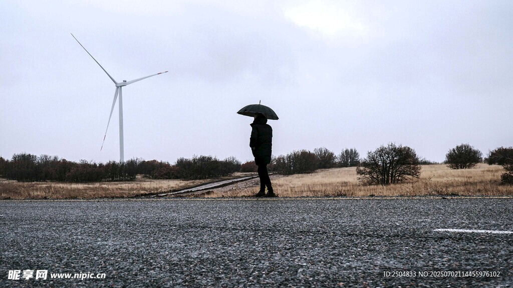 雨中撑伞人旁的风力发电机