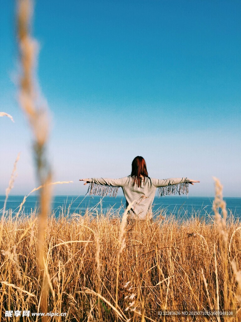 女子于金黄草地面向大海