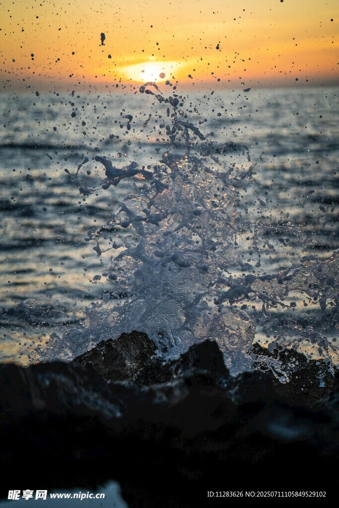 夕阳下海浪拍打礁石瞬间