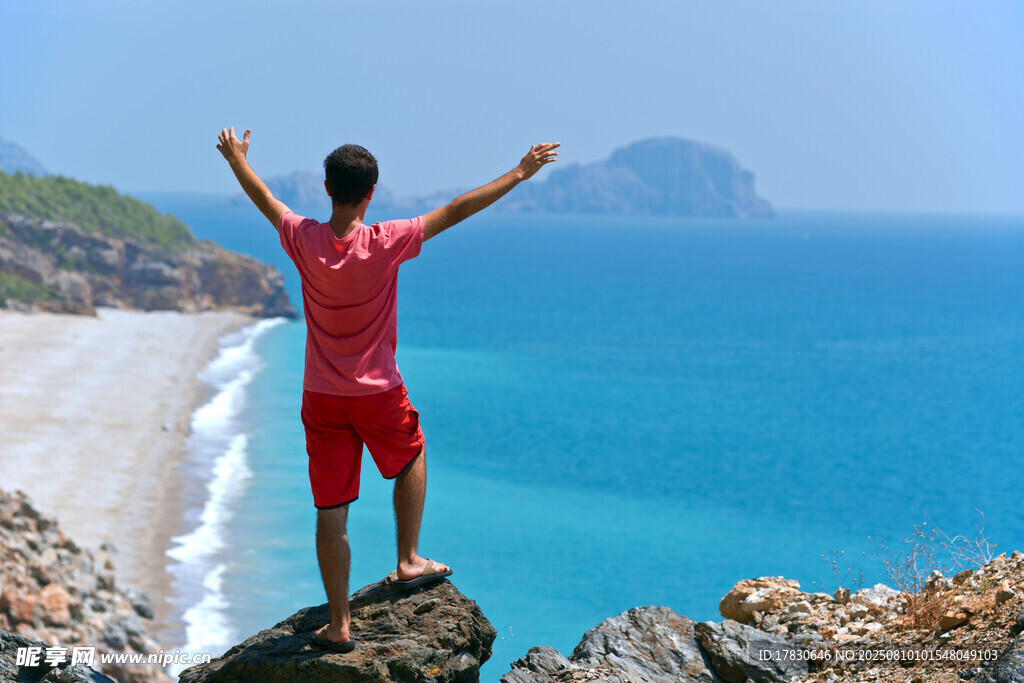 男子崖边舒展双臂赏海景