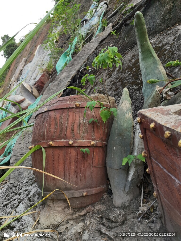 废弃木桶雕塑置于山坡绿植间
