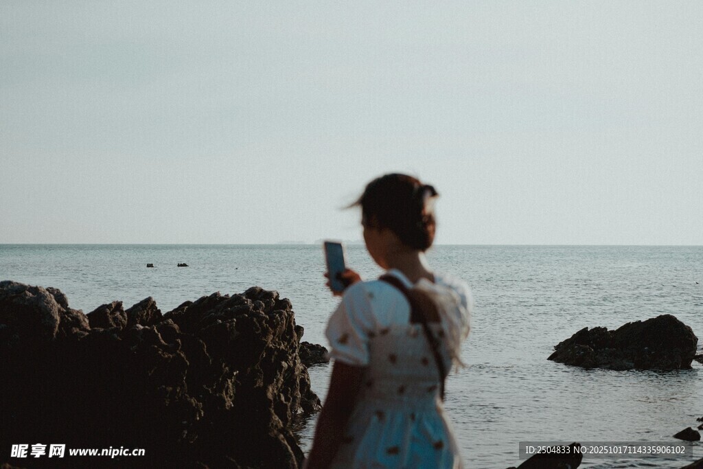 海边女子手持相机的背影
