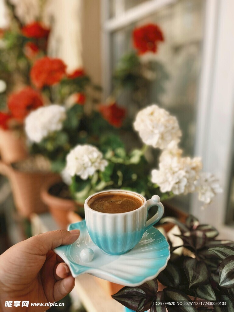 手捧蓝杯咖啡于花卉间