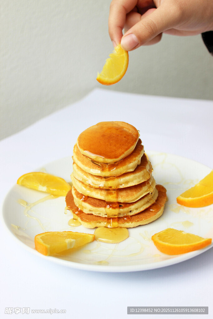 手放橙片于堆叠煎饼上