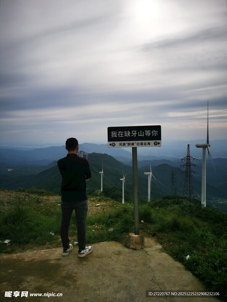 男子立于山顶路标旁观景