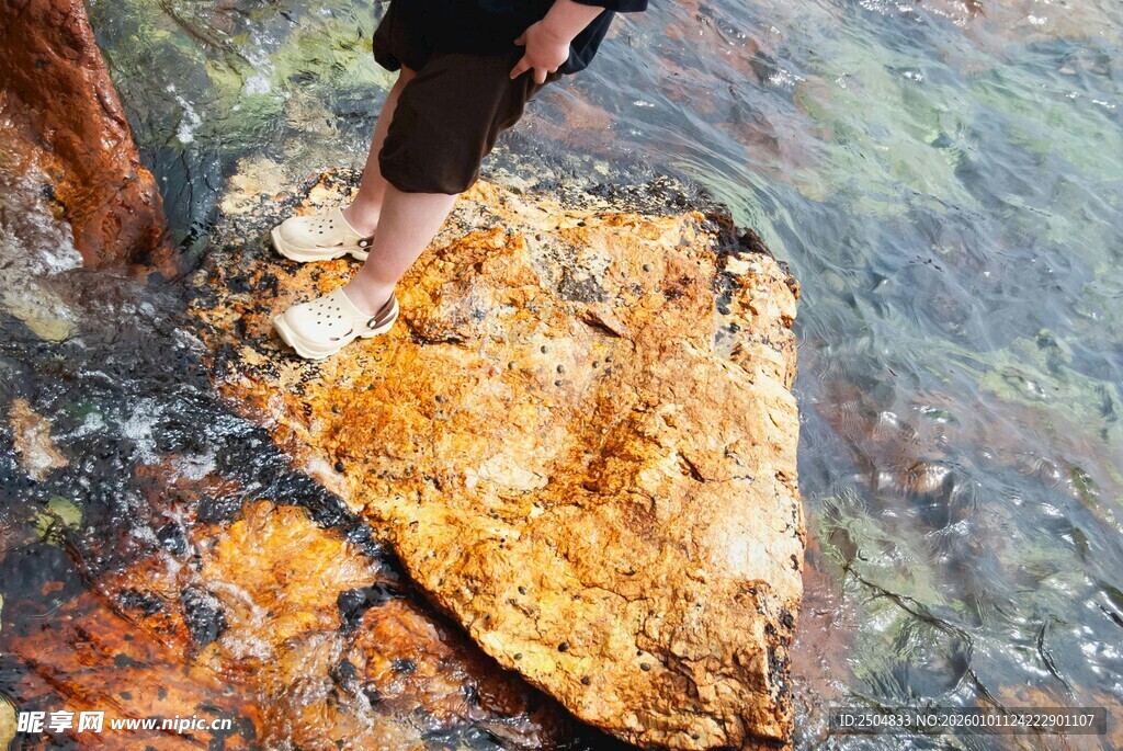 人立于水中斑斓岩石之上