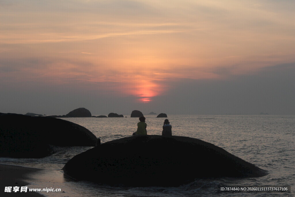 夕阳下海边礁石上的情侣