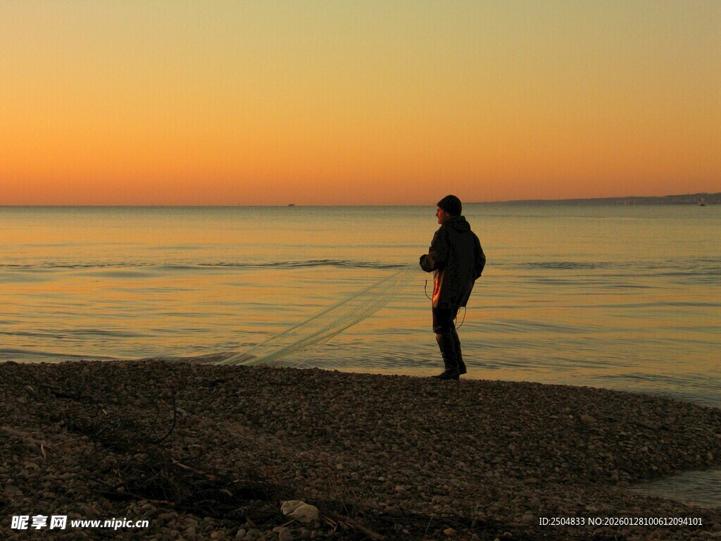 夕阳下海边撒网的捕鱼人
