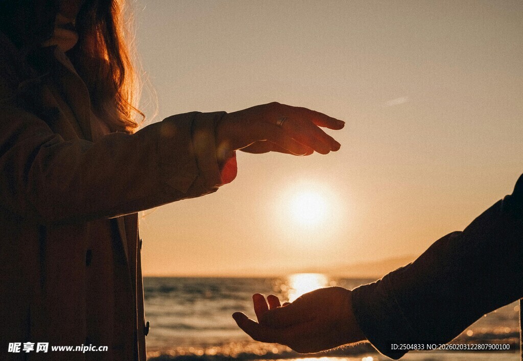 夕阳下两人海边伸手互动