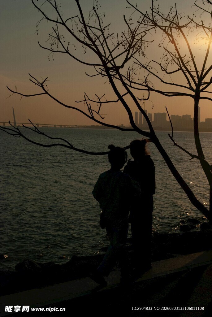 夕阳下情侣海边依偎剪影