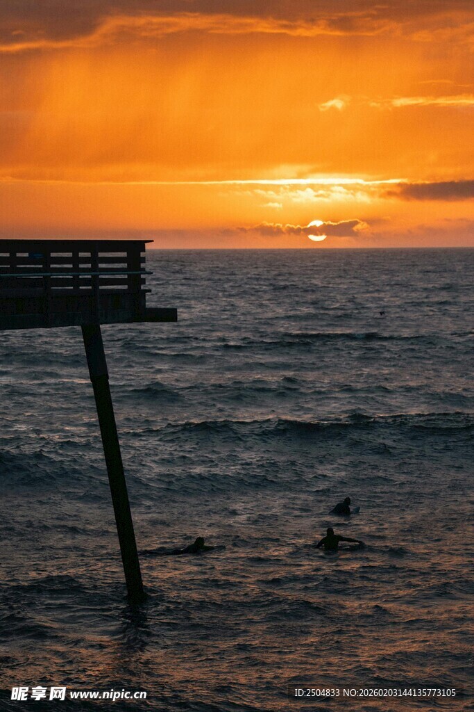 夕阳下的海边栈桥与冲浪者