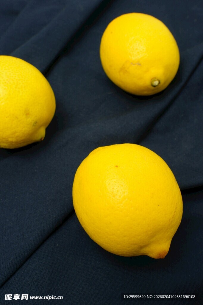 三颗鲜黄柠檬置于深色布上