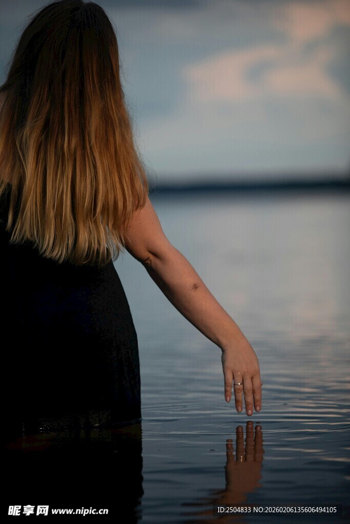 女子水边伸手触水的背影