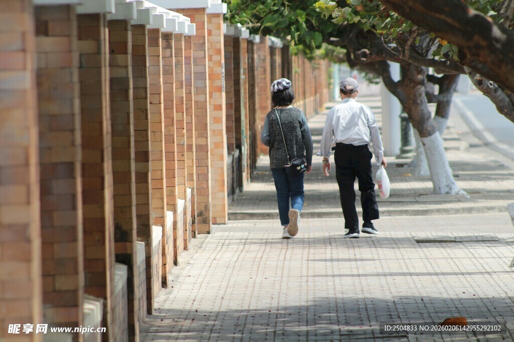 两人漫步于砖墙旁小道
