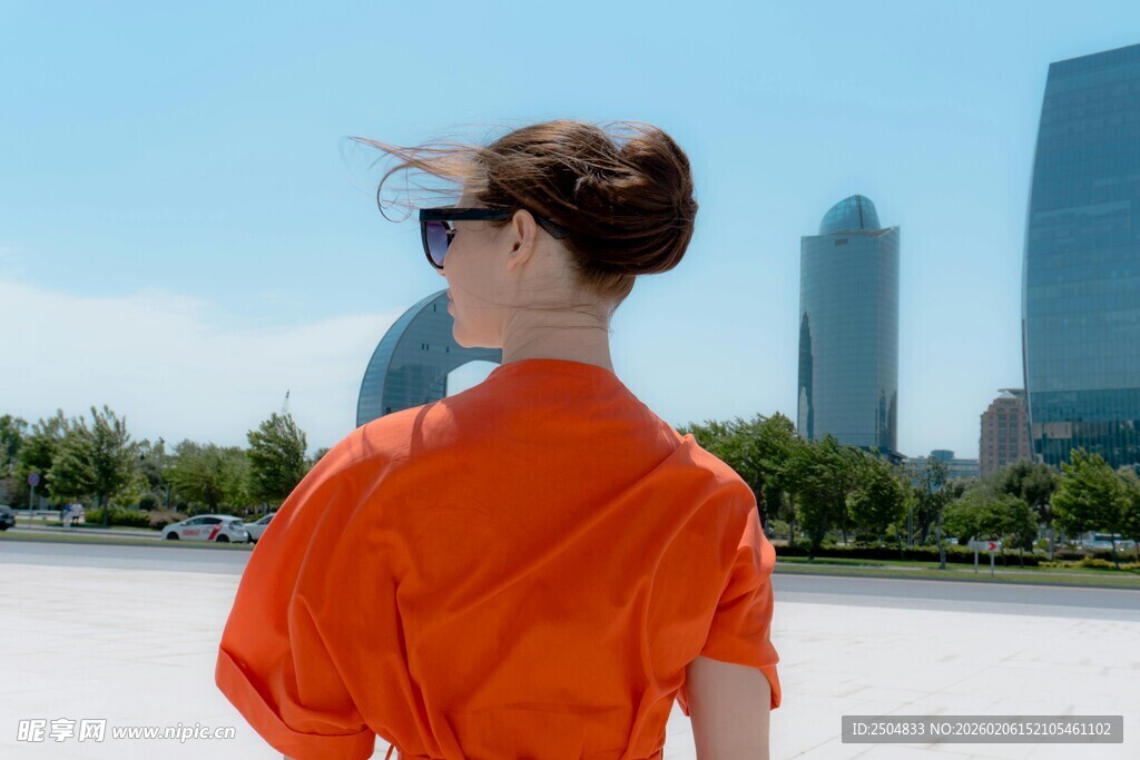 橙衣女士背对高楼赏景