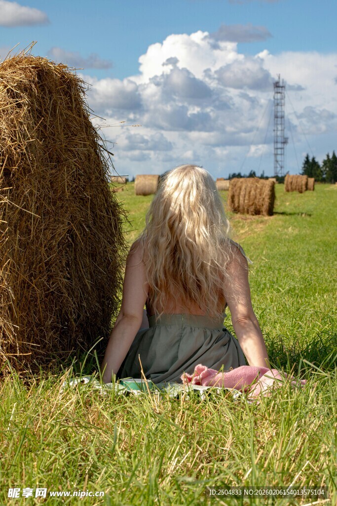 草地上背靠草垛的金发女子