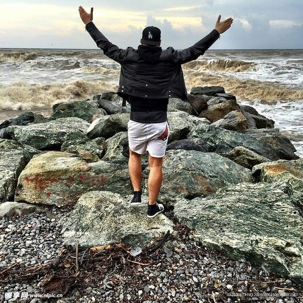 海边岩石上张开双臂的人