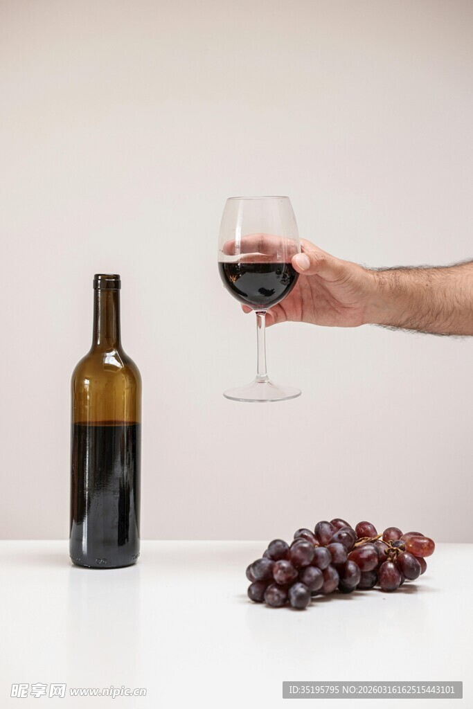 手擎红酒杯与葡萄和酒瓶