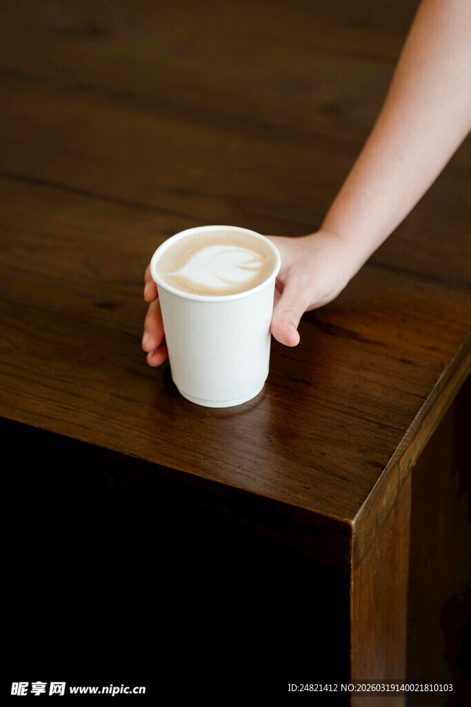 手托咖啡杯于木质桌面上