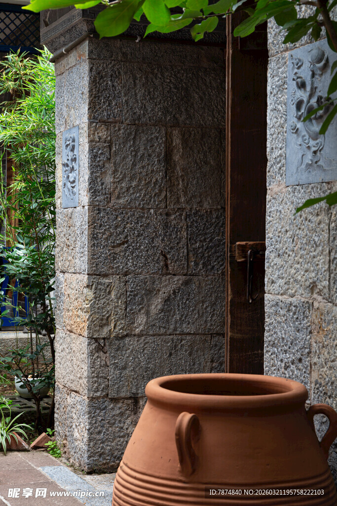 古朴陶缸置于石墙庭院旁
