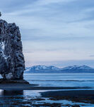 海边孤岩与远处雪山美景