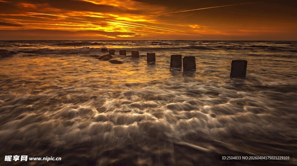 夕阳下海浪拍击岸边木桩