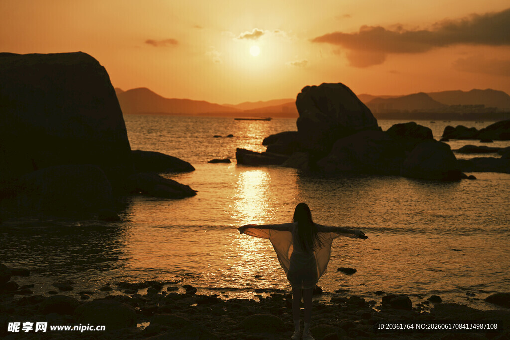 夕阳下海边伸展双臂的人