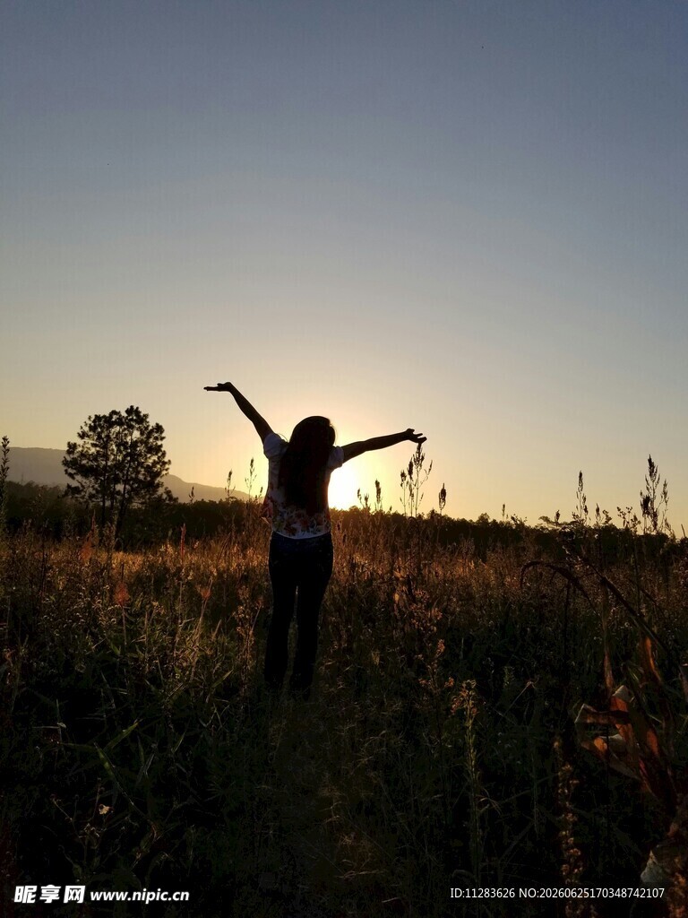 夕阳下田野中张开双臂的人