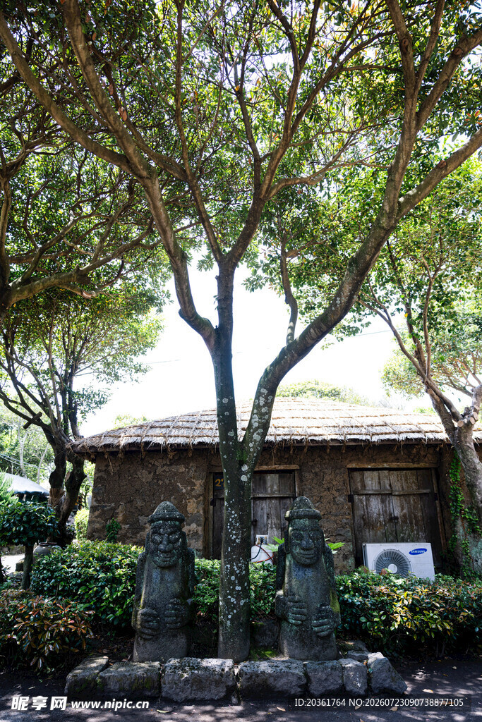 绿荫下的古朴小屋与石像