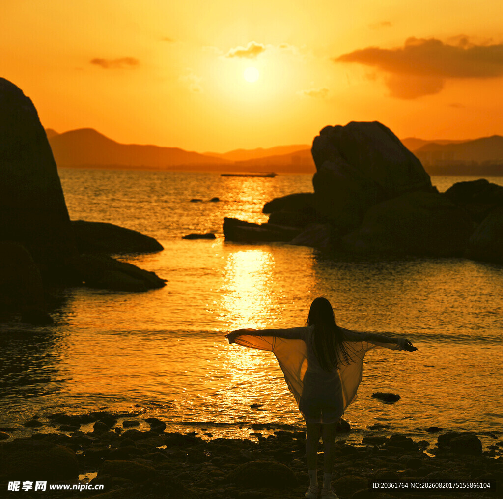 夕阳下海边伸展双臂的身影