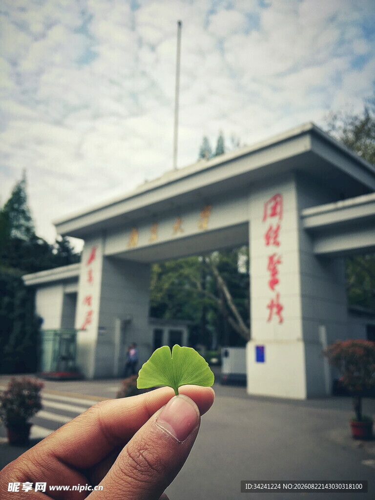 手持绿叶前的校园大门