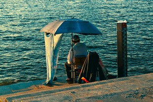 海边垂钓者撑伞静候鱼儿