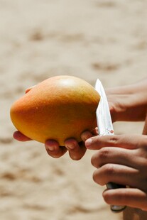 沙滩上手握芒果与刀