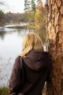女子倚树望宁静湖水