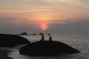 夕阳下海边礁石上的情侣