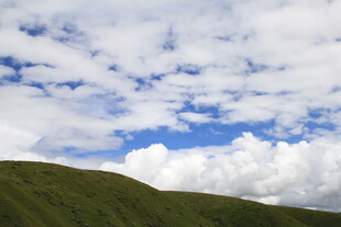 蓝天白云下的翠绿山坡