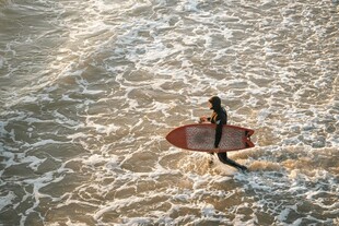 海边冲浪者持板踏浪前行