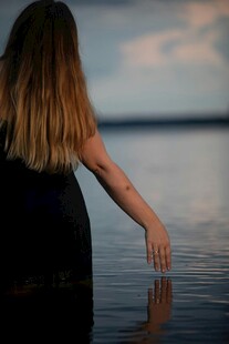 女子水边伸手触水的背影