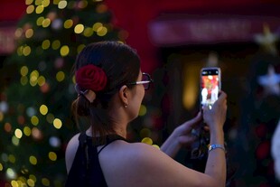 女子手持手机拍摄圣诞树