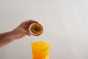 手递百香果至橙色饮品