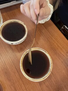 手搅木桌中的两杯深色液体